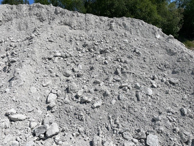 Grå hög av betongkross med ojämn yta, synlig stenstruktur och gröna träd i bakgrunden.