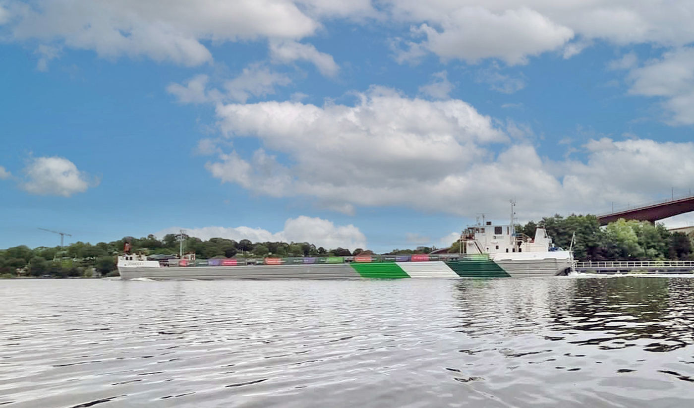 Ett fraktfartyg med Heidelberg Materials färger seglar under Årstabrin under en blå himmel.