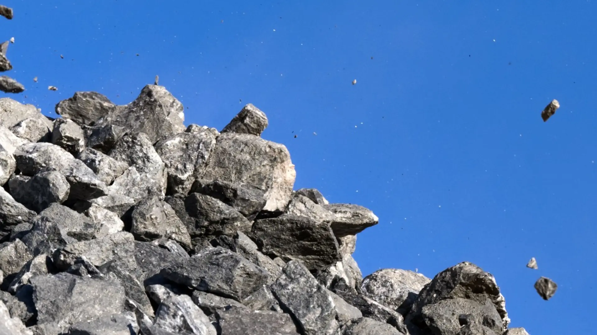 Stenblock som faller från en grushög mot en klarblå himmel. stenen i olika storlekar spridda i luften till höger om högen.