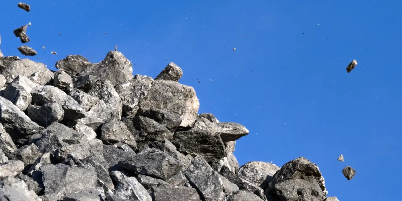 Stenblock som faller från en grushög mot en klarblå himmel. stenen i olika storlekar spridda i luften till höger om högen.