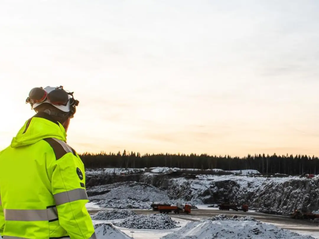 En person i gul skyddsutrustning står vid en stenbrott med snö och skog i bakgrunden.