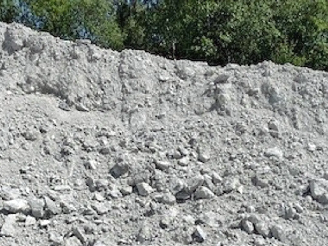 Grå hög av betongkross med ojämn yta, synlig stenstruktur och gröna träd i bakgrunden.