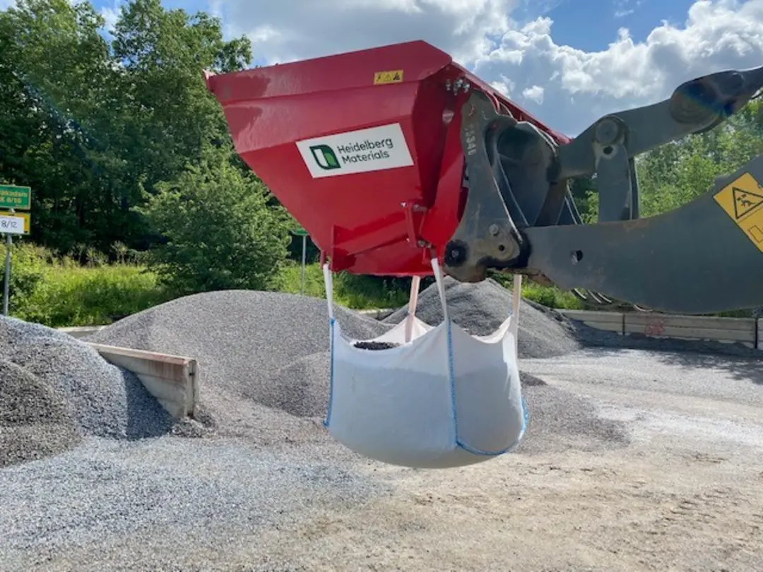 En maskin fyller en stor säck med grus på en industriell anläggning utomhus.