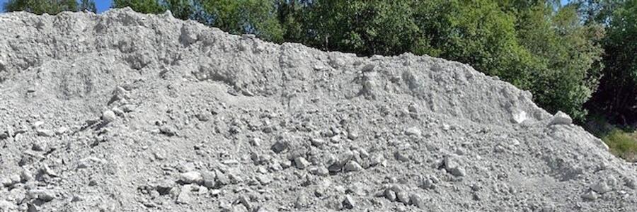 Grå hög av betongkross med ojämn yta, synlig stenstruktur och gröna träd i bakgrunden.