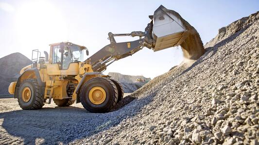 A loader transfers gravel onto a large pile at an industrial site under clear skies.